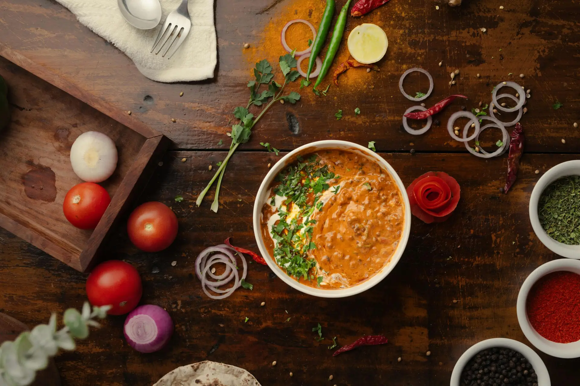 A vibrant top-down view of a flavorful Indian curry surrounded by fresh vegetables and spices.